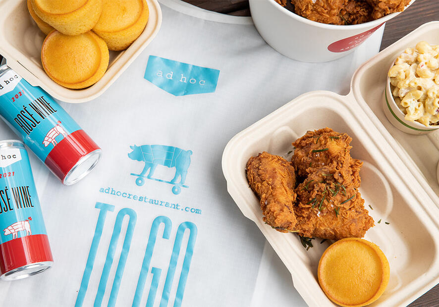 A collection of fried chicken and cornbread scattered on a picnic table with a white bag underneath.